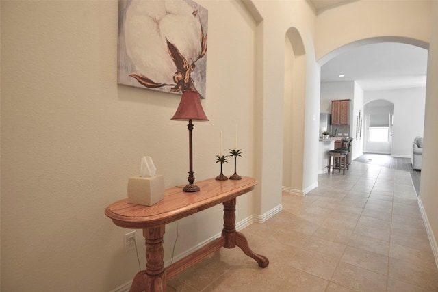 hallway featuring light tile patterned floors, arched walkways, and baseboards