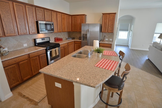 kitchen featuring arched walkways, appliances with stainless steel finishes, brown cabinetry, and a sink