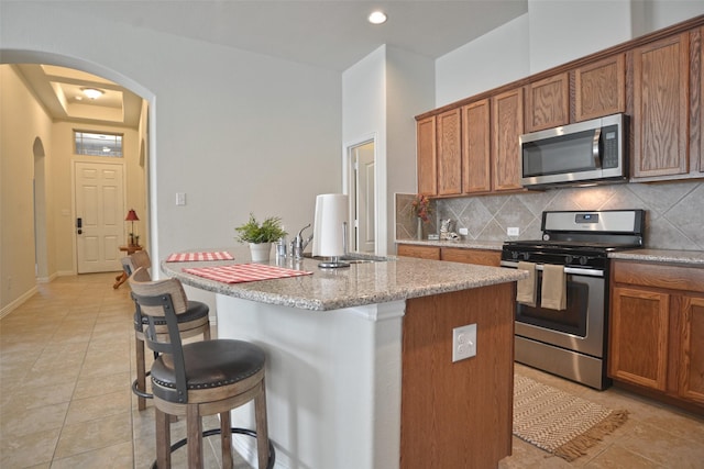 kitchen featuring arched walkways, a breakfast bar area, stainless steel appliances, and backsplash