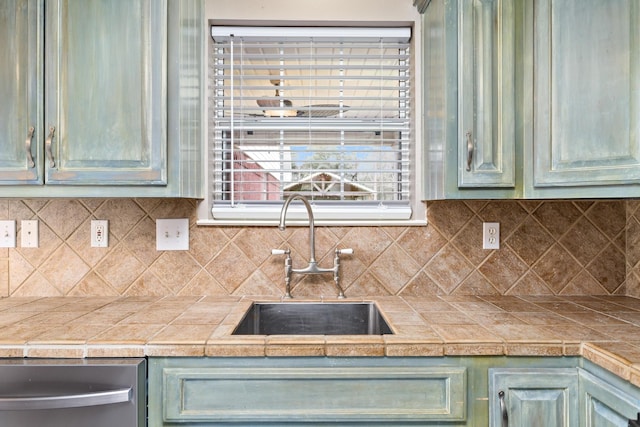 kitchen with stainless steel dishwasher, green cabinetry, decorative backsplash, and a sink