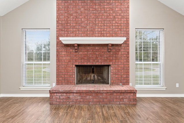 unfurnished living room featuring lofted ceiling, a fireplace, baseboards, and wood finished floors