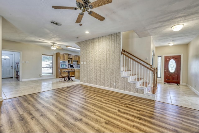 foyer entrance with visible vents, a textured ceiling, light wood finished floors, baseboards, and stairs