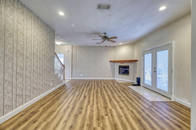 unfurnished living room with wallpapered walls, baseboards, a tile fireplace, french doors, and wood finished floors