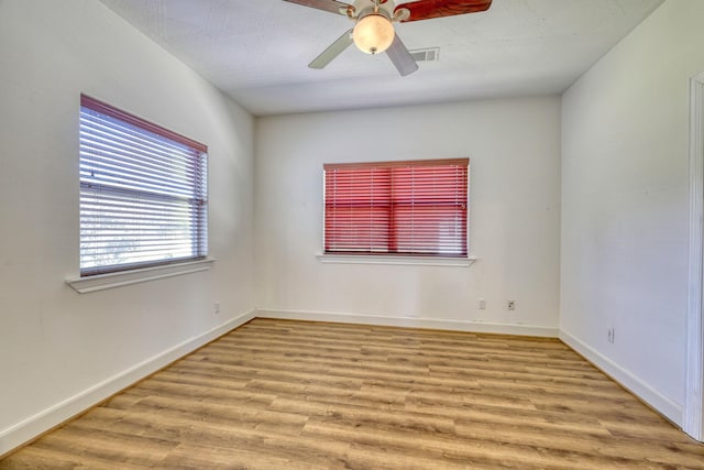 empty room with a ceiling fan, wood finished floors, visible vents, and baseboards