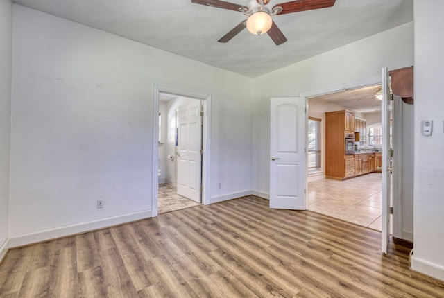 unfurnished bedroom featuring ceiling fan, baseboards, light wood-style flooring, and ensuite bathroom