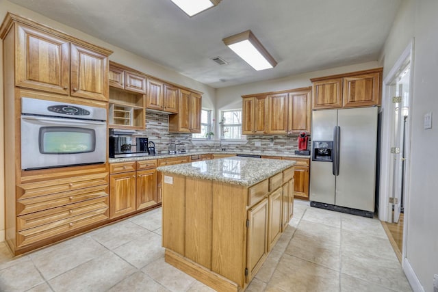 kitchen with a kitchen island, light stone counters, light tile patterned floors, decorative backsplash, and stainless steel appliances