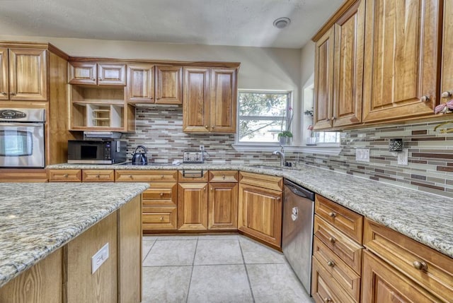 kitchen featuring light tile patterned floors, light stone countertops, stainless steel appliances, and a sink