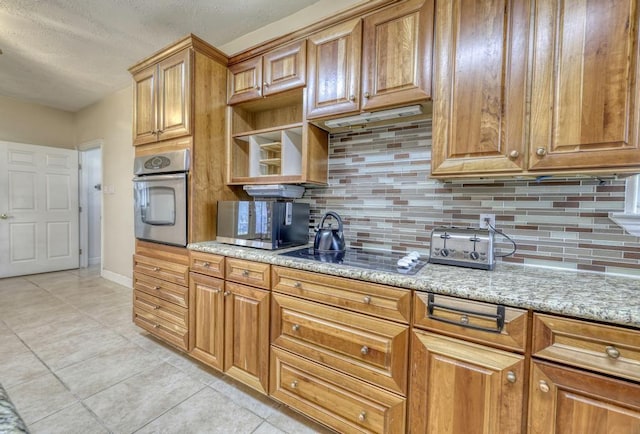 kitchen featuring tasteful backsplash, light stone countertops, light tile patterned floors, brown cabinets, and appliances with stainless steel finishes