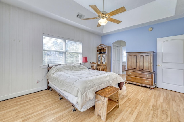 bedroom featuring visible vents, a tray ceiling, arched walkways, light wood-style floors, and baseboards