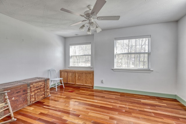 living area featuring a ceiling fan, baseboards, and light wood finished floors