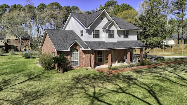 traditional-style home featuring brick siding, fence, a front yard, and roof with shingles