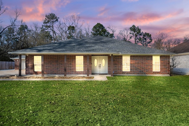 ranch-style house with covered porch, a shingled roof, a lawn, and brick siding