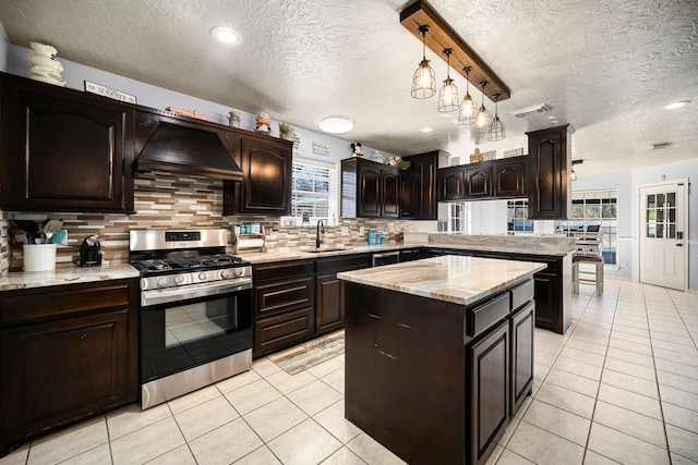 kitchen with custom exhaust hood, light tile patterned floors, tasteful backsplash, a sink, and stainless steel gas range oven