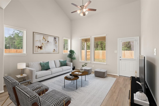 living area with high vaulted ceiling, light wood-type flooring, baseboards, and a ceiling fan