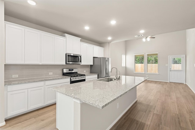 kitchen with tasteful backsplash, a center island with sink, white cabinets, appliances with stainless steel finishes, and a sink