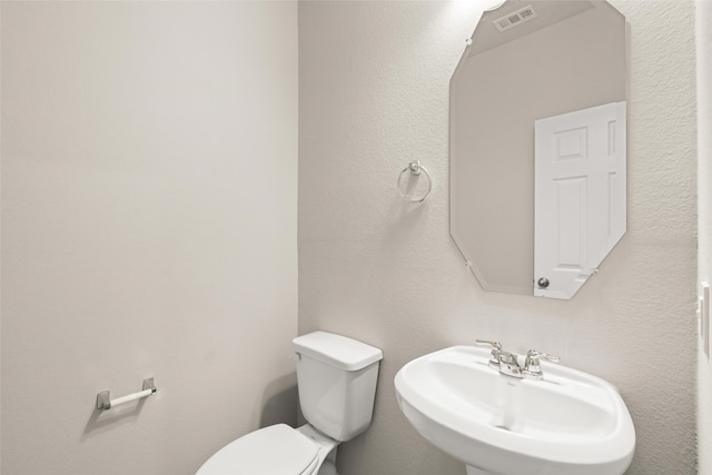 half bathroom featuring toilet, visible vents, and a sink