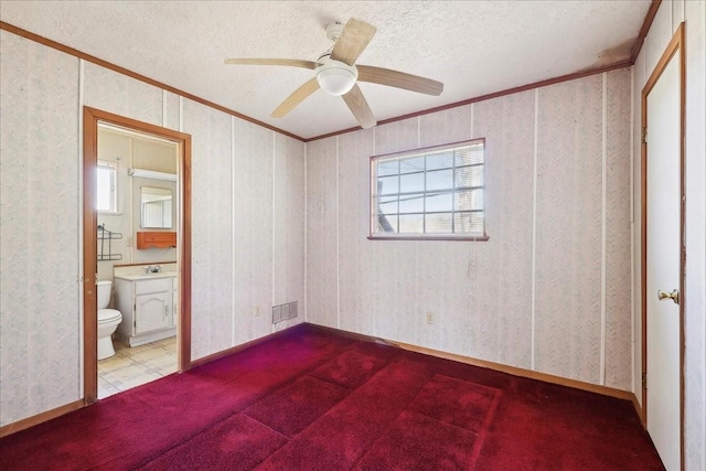 unfurnished bedroom with a textured ceiling, ensuite bathroom, visible vents, ornamental molding, and wallpapered walls