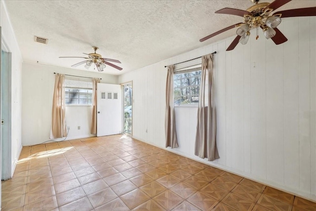 empty room featuring a textured ceiling, a ceiling fan, visible vents, and a healthy amount of sunlight