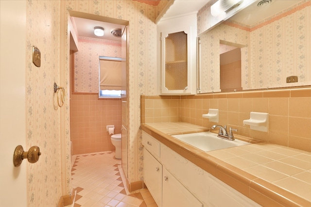 bathroom with wallpapered walls, toilet, a wainscoted wall, tile patterned flooring, and tile walls