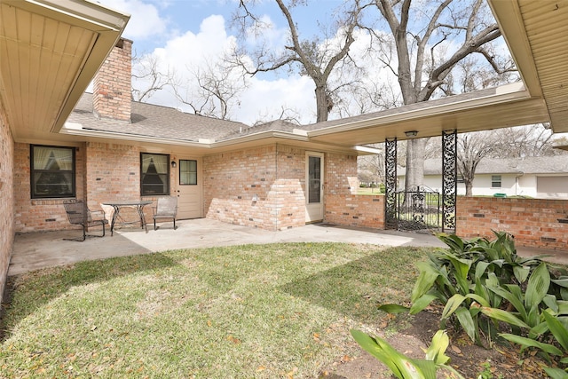 rear view of house featuring a lawn, a chimney, roof with shingles, a patio area, and brick siding