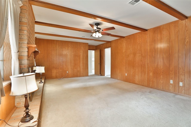 carpeted spare room featuring ceiling fan, wooden walls, visible vents, and beamed ceiling