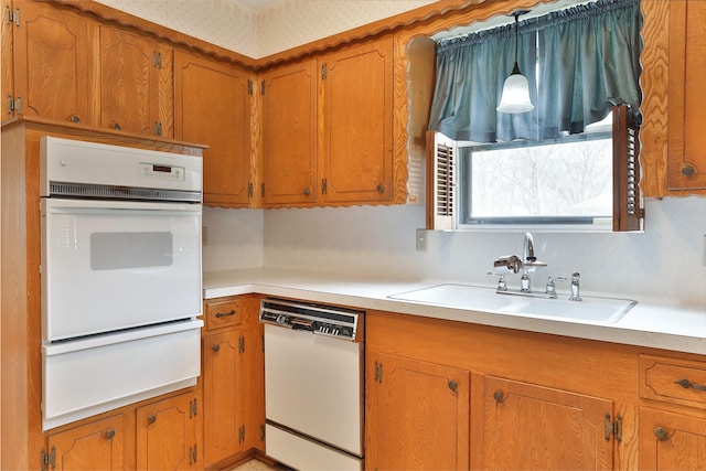 kitchen featuring white dishwasher, a sink, light countertops, a warming drawer, and brown cabinetry