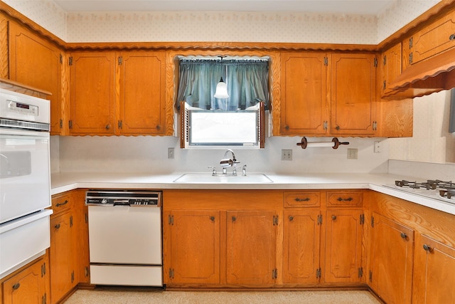 kitchen featuring white appliances, brown cabinetry, a sink, and light countertops