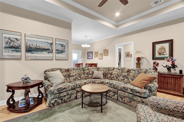 living area featuring a tray ceiling, crown molding, visible vents, wood finished floors, and ceiling fan with notable chandelier