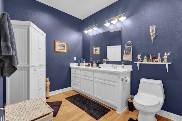 bathroom featuring double vanity, wood finished floors, toilet, and baseboards