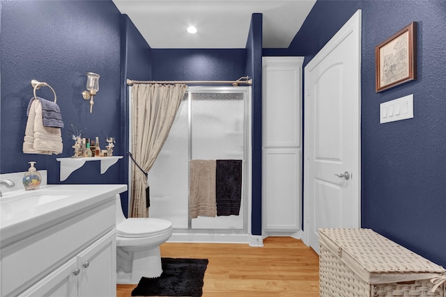 full bath with a textured wall, toilet, a stall shower, vanity, and wood finished floors