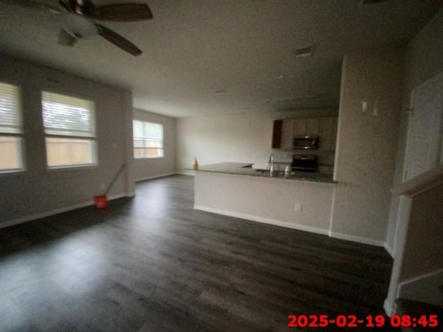 unfurnished living room with a sink, a ceiling fan, baseboards, and dark wood-style flooring