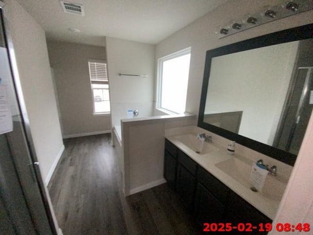 full bathroom featuring a garden tub, double vanity, visible vents, a sink, and wood finished floors