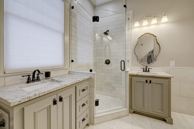 bathroom with tile walls, two vanities, a stall shower, and a sink