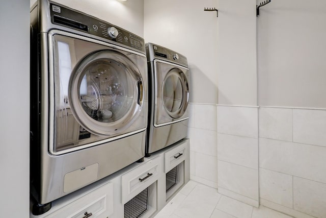 washroom featuring washer and dryer, laundry area, light tile patterned floors, and tile walls