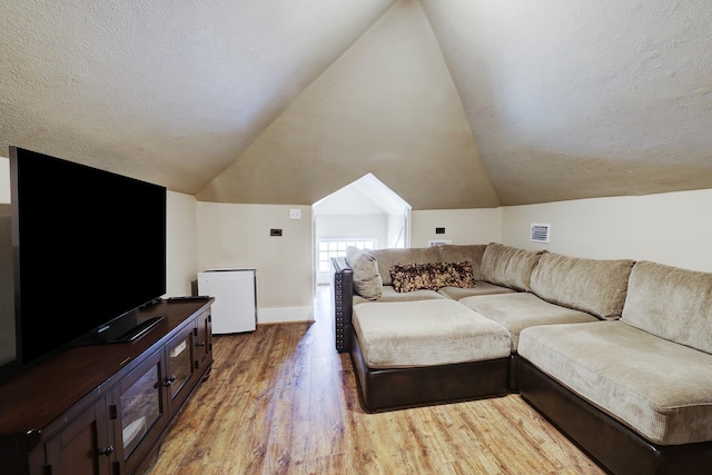 living area with vaulted ceiling, light wood-style flooring, visible vents, and a textured ceiling