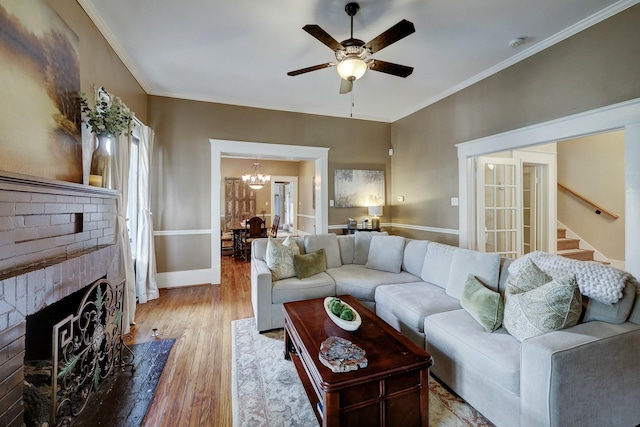 living area with ceiling fan with notable chandelier, ornamental molding, stairs, and light wood finished floors