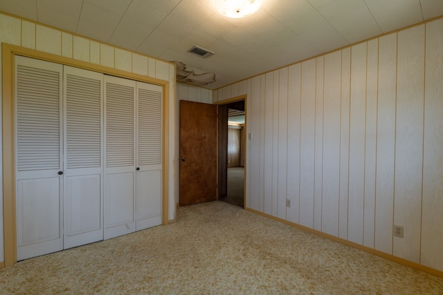 unfurnished bedroom with a closet, visible vents, carpet flooring, wooden walls, and baseboards