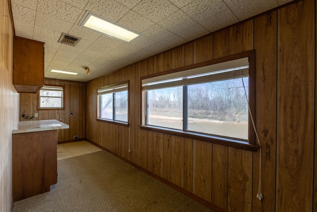 kitchen with wood walls, carpet flooring, visible vents, and brown cabinets