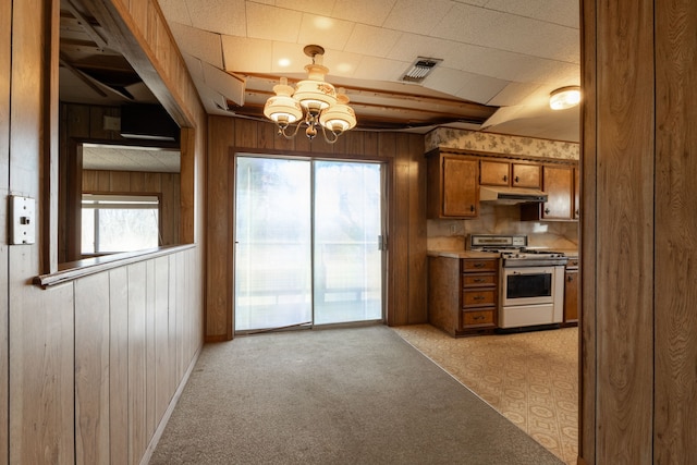 kitchen featuring wooden walls, light colored carpet, visible vents, range with gas stovetop, and brown cabinetry