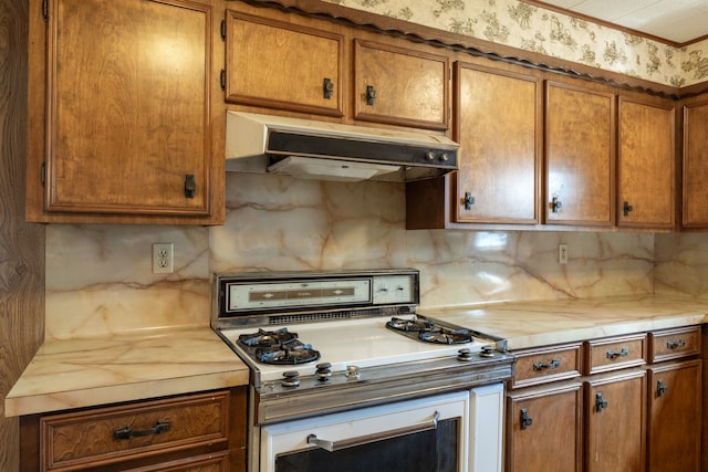 kitchen with brown cabinets, under cabinet range hood, range with gas stovetop, and backsplash