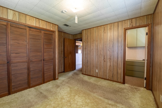 unfurnished bedroom with wooden walls, carpet flooring, visible vents, baseboards, and a closet