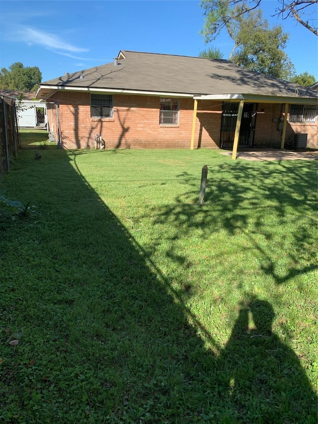 rear view of house with a yard, brick siding, cooling unit, and fence