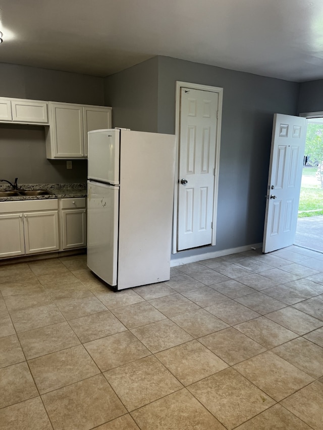 kitchen featuring baseboards, white cabinets, dark countertops, freestanding refrigerator, and a sink