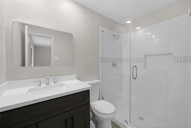 bathroom featuring a stall shower, a textured wall, vanity, and toilet