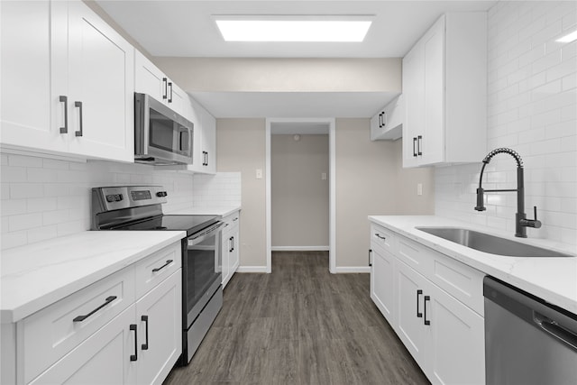 kitchen with light stone counters, appliances with stainless steel finishes, dark wood-type flooring, white cabinets, and a sink