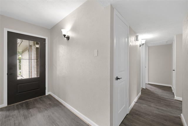 foyer featuring dark wood-style floors, a textured wall, and baseboards