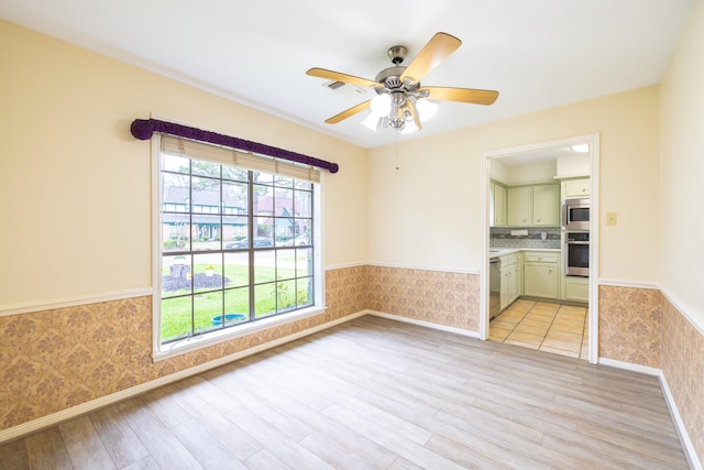 empty room with visible vents, light wood-style floors, wainscoting, ceiling fan, and wallpapered walls