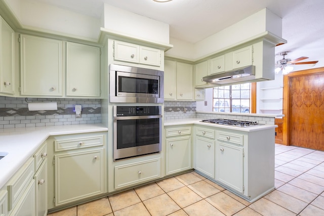 kitchen with a peninsula, under cabinet range hood, stainless steel appliances, and light countertops