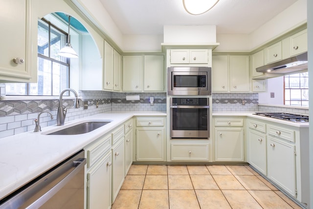 kitchen featuring light countertops, backsplash, appliances with stainless steel finishes, a sink, and under cabinet range hood