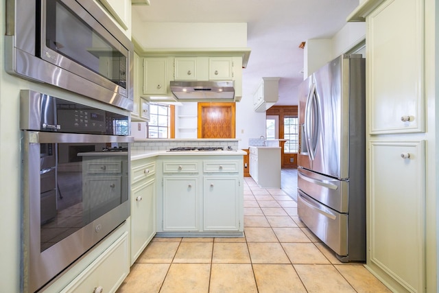 kitchen with light tile patterned floors, light countertops, appliances with stainless steel finishes, a peninsula, and under cabinet range hood